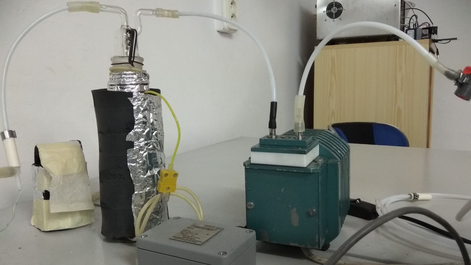 Laboratorní sestava pro zkoušky sorpce: otápěná skleněná promývačka s termočlánkem, hadičky a membránové čerpadlo na laboratorním stole.